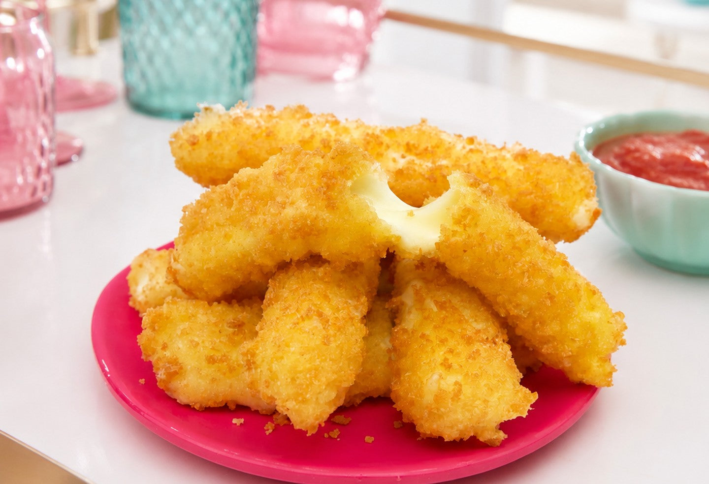 Tempura cheese sticks on a pink plate with marinara