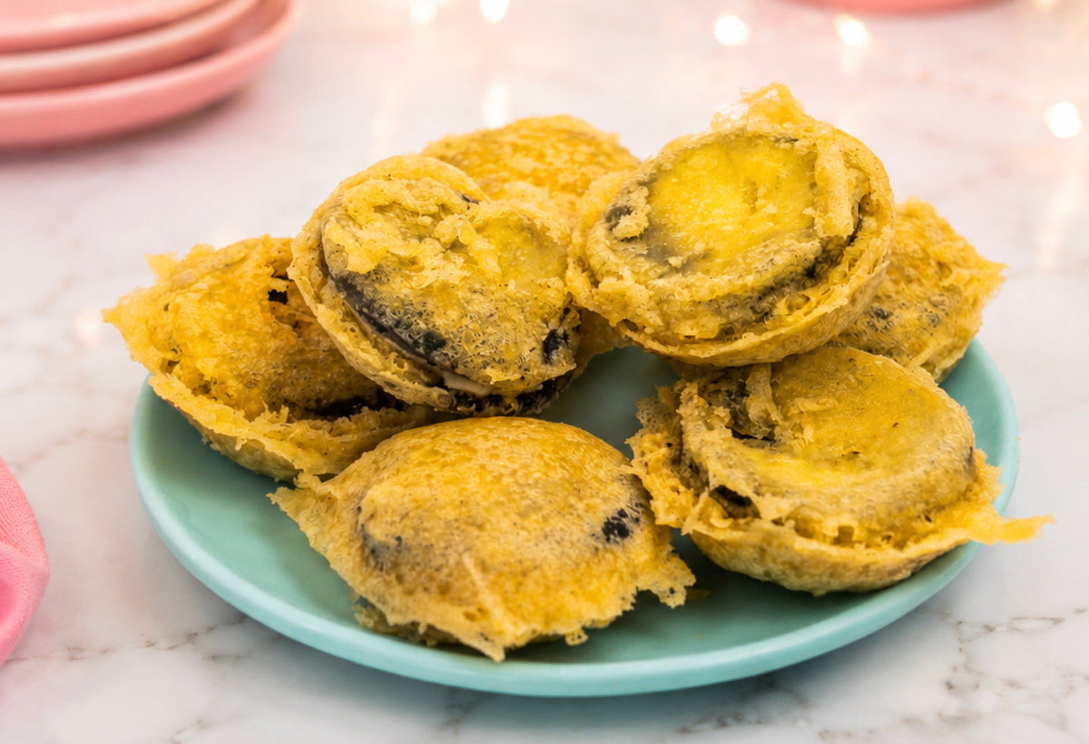 Golden tempura fried Oreos stacked on a mint plate with pink dessert plates and fairy lights