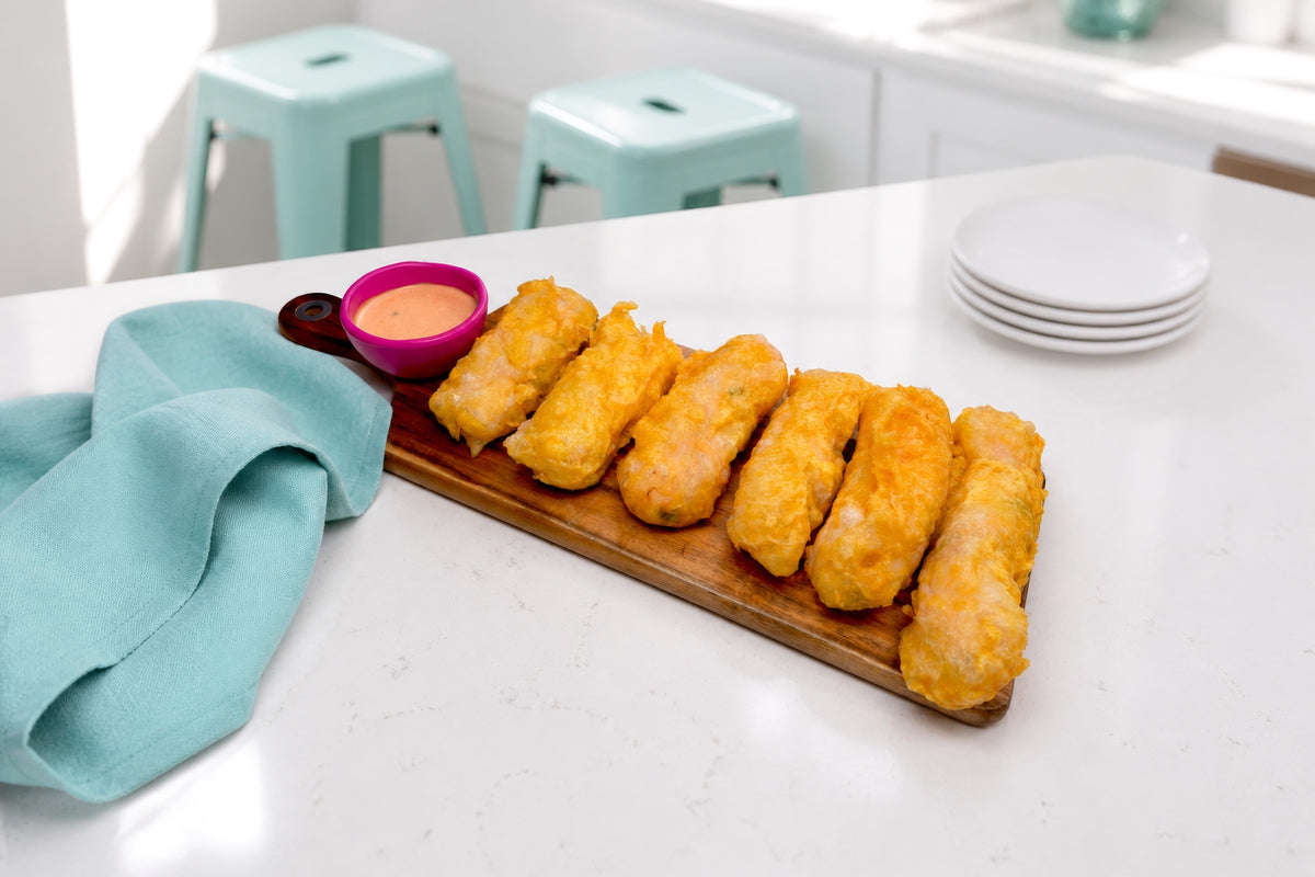 Golden spicy shrimp tempura spring rolls arranged on a wooden board with spicy mayo in a bright kitchen.
