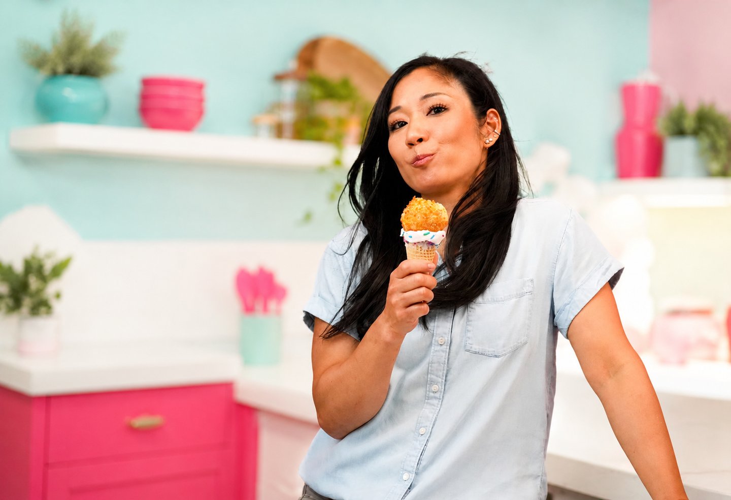 Woman holding a tempura ice cream cone with rainbow sprinkles in a pastel kitchen.