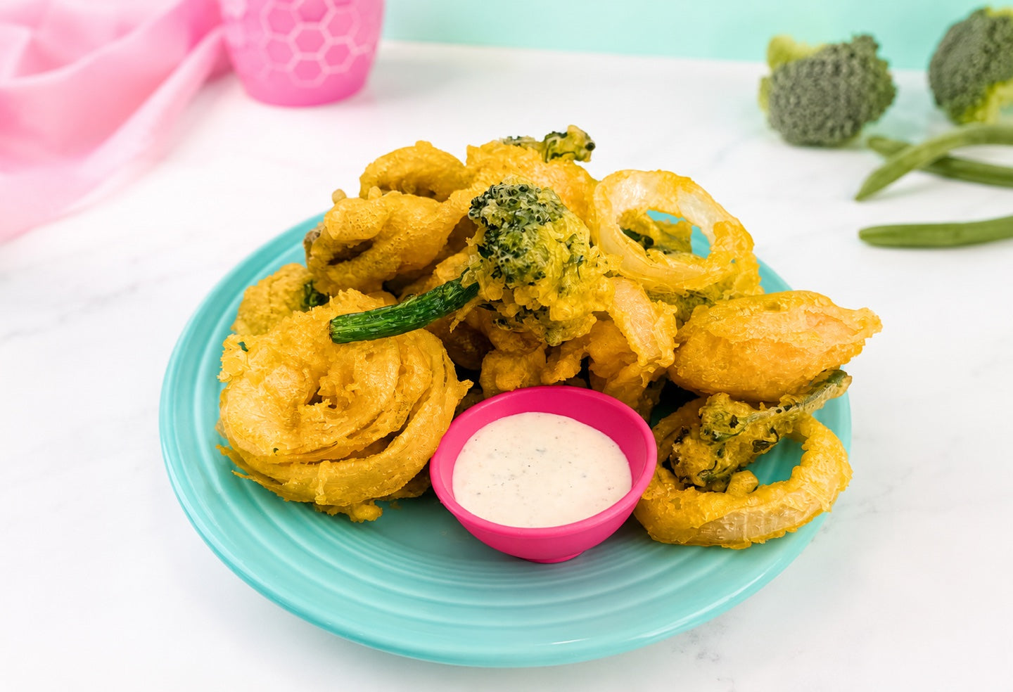 Golden tempura mushrooms, broccolini, and onion rings on a turquoise plate with dipping sauce.